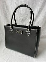 Front and side view of black Kate Spade Wellesley Quinn tote showing overall structure, handles, stitching, and hardware.