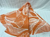 Towel partially unfolded showing orange background with white tropical floral and leaf print