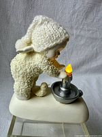 Figurine rear view showing knit hat, bird, lit candle