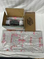 Overview of lot with open box of bubble-wrapped parts, hardware tub, separate boxed rack, flat wrapped panels