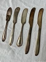 Front view of all five butter knives showing size and pattern variety