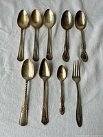 Full group of nine mixed silverplate flatware items laid out