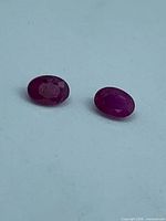 Two oval faceted rubies on light surface