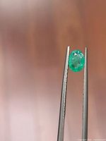 Front view of oval emerald held by tweezers