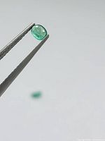 Emerald held in tweezers, second gemstone blurred in background