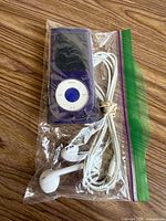 Front view of iPod nano in purple iSkin Duo case with earbuds, all in zipper bag