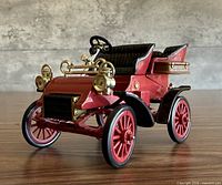 Front left perspective of red 1903 Ford Model A diecast car with gold lamps and red wheels