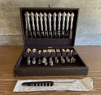 Open wooden case showing 12 knives in lid and remaining flatware pieces in base
