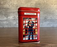 Front view of red telephone booth tin showing figure inside and TELEPHONE sign