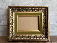 Front view of wooden frame showing gold gilt carved design and olive velvet border