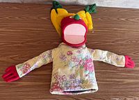 Front view of full puppet showing floral body, red head, yellow yarn hair, red hands