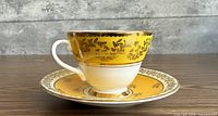 Side view of teacup on saucer showing yellow ground and gold filigree