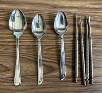 Three teaspoons and three nut picks laid out on wood surface