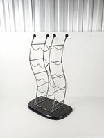 Front three-quarter view of chrome wave wine rack showing curved frame, black finials, and base
