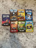 Front covers of seven Dog Man hardcover books arranged on floor