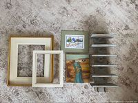 All items laid out: two empty frames, painting, cross-stitch, curio shelf