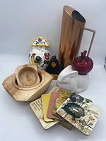 All items arranged together including ceramic rooster planter, rabbit candle holder, wood bird figurine, copper pitcher, glass apple, wood bowls, decorative coasters