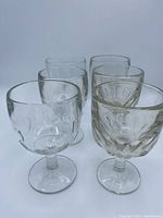 Front view of six clear glass goblets showing both optic dimple and faceted swirl patterns
