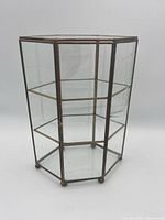 Full view of hexagonal glass display case showing brass frame and shelves