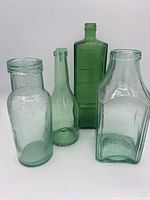 Group shot of the four aqua/green glass bottles showing their differing shapes and embossed details