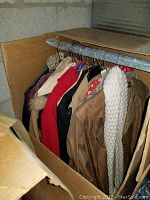 Photo showing a rack with a variety of vintage coats and jackets on hangers, including tan trench coat, red wool coat, white quilted jacket, and others.