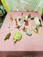 Overview of vintage glass figurines, turtle figurines, brass birds, and other small collectibles on pink fabric surface