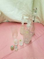 Photo of four assorted glass decanters with glass stoppers and two glass salt and pepper shakers with metal tops on a pink surface.