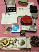 Various vintage collectible items including coins, jewelry, and boxed accessories arranged on a pink cloth background.