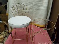 Chair with white padded seat and decorative gold-tone metal back, beside a matching circular gold-tone metal stand without glass top