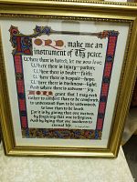 Framed serigraph showing prayer text with decorative illuminated manuscript style border in gold, red, blue, and black hues.