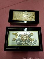 Two rectangular jewelry boxes placed on a pink surface, viewed from above showing their decorative lids.