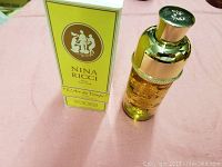 Photo of the vintage Nina Ricci L'Air du Temps perfume bottle and its original box on a pink fabric surface.