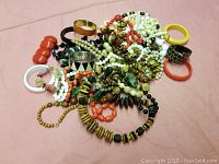 Wide view of assorted costume jewelry pieces including bead necklaces and colorful bangles on a pink background.