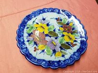 Front view of the ceramic decorative plate showing the hand-painted floral design with yellow, purple and pink flowers and the blue scalloped border.