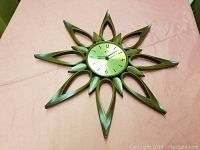 Front view of the large vintage Syroco sunburst wall clock with wooden-look frame and gold clock face on pink background.