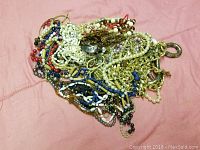 Top view of tangled assorted beaded and chain necklaces on pink fabric background.