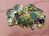 Top view of assorted jewelry parts and components showing variety of pendants, charms, and small chains on a pink background.