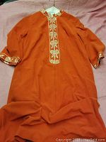 Full view of the orange dress laid flat with visible embroidery on the cuffs, front placket, and collar.