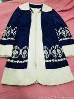 Full view of vintage blue and cream jacket laid flat showing embroidery and zipper front.