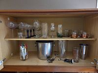 Overview of entire lot inside cabinet, showing glassware, copper mugs, stainless ice bucket and bar tools