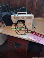 Sewing machine with foot pedal, cords, carrying bag and instruction book on table