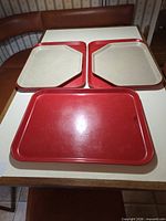 Five plastic cafeteria trays on table: three red rectangular, two grey trapezoid