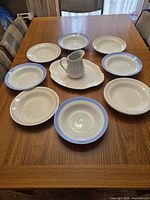 Eight bowls/plates, white platter in centre with creamer on wooden table