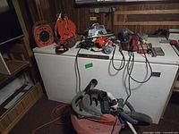 Assorted electrical tools on freezer top with shop vacuum in foreground
