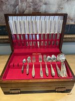 Open wooden chest displaying knives in lid and assorted flatware in red felt interior