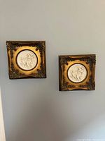 Both square gold framed bisque plaques hanging on wall