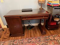 Front angled view showing entire desk, glass top, drawer, cabinet door, column support