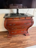 Front view of bombe chest showing marble top, drawers, hardware and TV stand placed on top