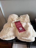 Top view of folded cream faux fur throw with tag and ribbon