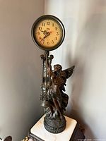 Front view of figural clock showing full sculpture, dial and pendulum